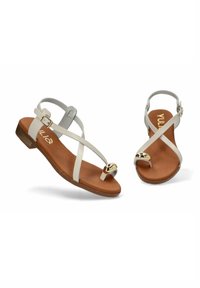 Sandalias blancas con un diseño de tiras cruzadas, una plantilla marrón y un acento dorado circular. Suela plana con hebillas ajustables.