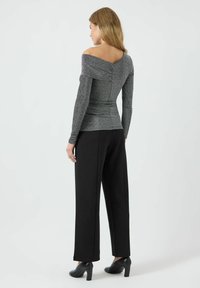 Sølvfarget off-shoulder topp med lange ermer, med rynket design og glatt tekstur, kombinert med høytaljede svarte bukser.