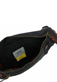 Zwarte nylon tas interieur met gouden rits, voorzien van een grijze stoffen label en een gele stofaccent. Gladde textuur, minimalistisch ontwerp.