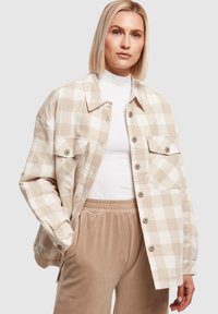 Veste-chemise en flanelle à carreaux beige avec un col, des boutons sur le devant et deux poches poitrine, assortie à un pantalon beige à taille élastique. Texture lisse.