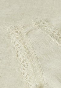 Tessuto di lino in bianco sporco con delicato pizzo sul bordo, caratterizzato da piccoli ritagli circolari lungo il margine, che mette in risalto una superficie morbida e testurizzata.