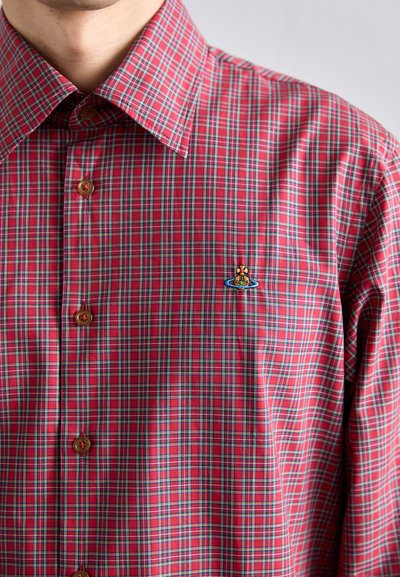 Rød rutete skjorte med knapper laget av stoff med blå og grønne detaljer. Har en liten brodert design nær brystet og brune knapper.