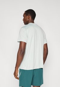 Ανοιχτό μέντας πράσινο κοντομάνικο μπλουζάκι απόδοσης με διακριτικό υφασμένο σχέδιο στον ώμο, συνδυασμένο με πετρόλ σόρτς που έχουν διακοσμητικό μοτίβο.