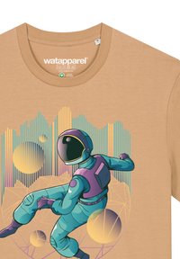 Beige T-shirt met een grafisch ontwerp van een astronaut in teal en paars, omringd door geometrische vormen en gouden sferen.