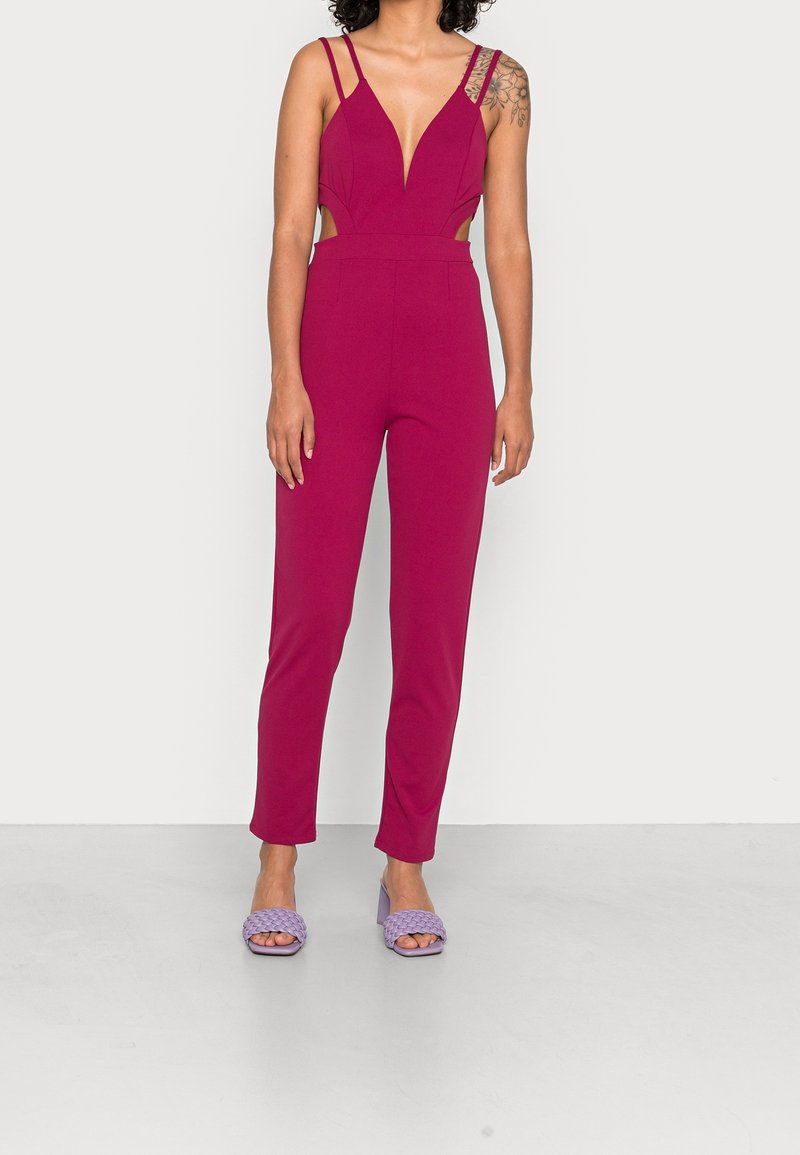 Jumpsuit fucsia con scollo a V profondo, lati a taglio e spalline sottili. Abbinato a sandali con tacco a blocco lavanda con design intrecciato.