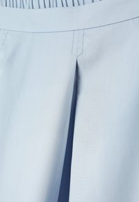 Tela azul claro con un pliegue central y costuras visibles cerca de una cintura fruncida, probablemente parte de una prenda.