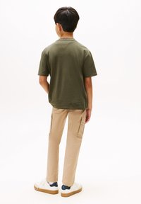 Olivgrön t-shirt med kort ärm, khakifärgade cargobyxor med sidofickor, vita sneakers, synlig marinblå och röd detalj på kragen.
