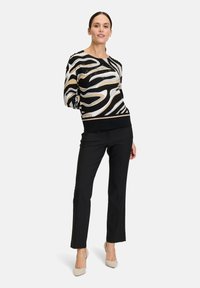 Schwarzer und cremefarbener gemusterter Pullover mit rundem Ausschnitt und Dreiviertelärmeln, kombiniert mit schwarzen geraden Hosen und beigen Absatzschuhen.