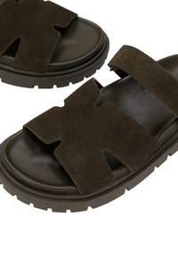 Sandales ouvertes en daim marron foncé avec larges brides et semelles en caoutchouc épaisses et texturées, conçues pour un usage décontracté.