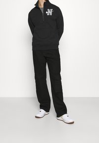 Black zip-up sweatshirt with embroidered letter logo, paired with black cargo pants featuring side pockets, and white sneakers.