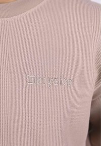 Pull à côtes rose clair avec un col rond et logo "Drugsize" brodé dans le même fil. Texture douce avec des détails subtils.