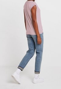 Pruhovaná triko s krátkým rukávem v světle růžové a bílé, spárované s volnými světle modrými džíny a bílými teniskami.