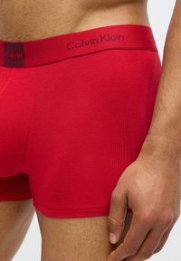 Boxer briefs de algodão vermelhos com uma cintura com logo; textura suave; design justo; detalhes de costura visíveis.