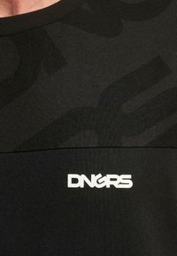 Musta crew neck -t-paita, joka on valmistettu teksturoidusta kankaasta, jossa on sävykkäitä kuvioita ja valkoinen "DNGRS" -logo rinnassa.