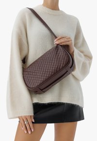 Borsa a tracolla in pelle marrone con texture trapuntata e design piatto, dotata di una lunga tracolla e leggere accentuazioni hardware.