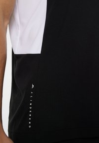 Svart och vit idrottströja med en färgblockdesign, logotypdetalj på sidan och en slät, lätt tygkvalitet.