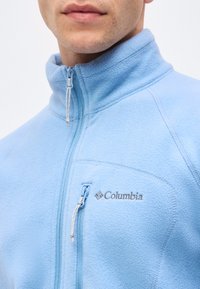 Άνδρας με ανοιχτό μπλε φλις μπουφάν Columbia με φερμουάρ στο στήθος και ψηλό γιακά.