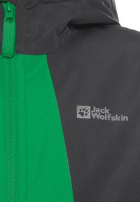 Zelená a tmavě šedá bunda se zipem vpředu a logem Jack Wolfskin na hrudi, vybavená zvýšeným límcem a kapucí.