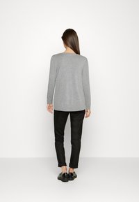 Grauer Pullover mit langen Ärmeln und rundem Hals, kombiniert mit schwarzen Hosen. Glatte Textur, lässige Passform, hinten etwas länger.