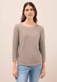 Helles graues langärmeliges Strickoberteil mit Rundhalsausschnitt, das ein strukturiertes Muster und einen lässigen Schnitt aufweist, kombiniert mit legeren blauen Jeans.