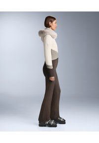 Testhez simuló síruha bézs és szürke kapucnis felsővel, texturált mintával, sötétbarna bővülő szárú nadrággal és fekete cipővel párosítva.