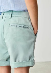 Mint green cotton shorts with a rolled cuff, featuring a back pocket label "BAKER BY TED BAKER" in navy blue. Smooth texture.