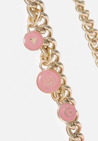 Collana in metallo dorato con accenti in smalto rosa. Presenta tre ciondoli rotondi: uno con "EST 1981", uno con "G" e uno con un triangolo rovesciato.