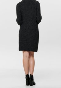 Abito a maglia grigio scuro con scollatura alta, che presenta una silhouette dritta e maniche lunghe, abbinato a stivaletti neri con tacco.