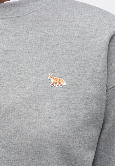 Sudadera gris con un pequeño zorro bordado en naranja y blanco en la parte izquierda del pecho. Tejido suave y texturizado con cuello redondo.