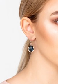 Csepp alakú fülbevalók facettált fekete kövel és rózsa arany szerelvényekkel. A kő egy textúrált fémkeretbe van foglalva.