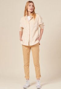 Lichtbeige corduroy shirtjack met twee borstzakken, gecombineerd met lichtbruine omgeslagen broek en witte sneakers. Eenvoudig en veelzijdig ontwerp.