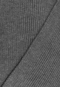 Grijze gebreide stof met een geribde textuur, met verticale lijnen en een soepele rand. Het materiaal lijkt zacht en flexibel te zijn.