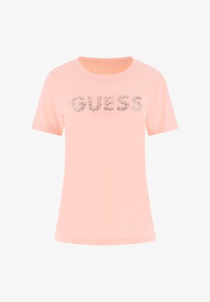 Šviesiai rožinė trumpomis rankovėmis marškinėliai su užrašu „GUESS“ dekoruotais rašmenimis ir „EST. 1981“ spausdinta po prekės ženklo pavadinimu.
