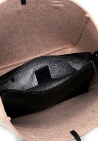 Szary, nieckowaty wnętrze torebki z czarną kieszonką na zamek. Teksturowana czarna podszewka z powtarzającym się wzorem. Miękki, minimalistyczny design.