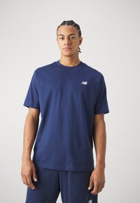 T-shirt en coton bleu marine avec un col rond et des manches courtes, arborant un petit logo blanc sur la poitrine gauche. Design simple.