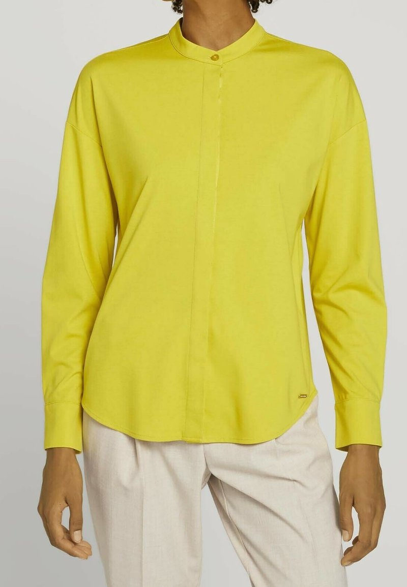 Chemise jaune à manches longues avec col officier, fermeture à boutons sur le devant et ourlet arrondi. Fabriquée en tissu lisse avec une coupe décontractée.