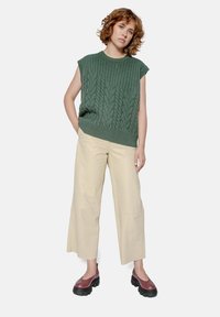 Green cable-knit sleeveless sweater, cream wide-leg trousers, and burgundy slip-on shoes. Smooth texture and relaxed fit.