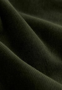 Tessuto a coste verde scuro con una consistenza morbida, che mostra una leggera lucentezza e pieghe ondulate, illustrando profondità e movimento.
