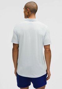 Jasnoniebieska koszulka polo z miękkiego materiały, z standardowym kołnierzykiem i krótkimi rękawami, wyeksponowana z tyłu, z minimalnym zdobieniem.