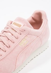 Tenisky Puma Roma v světlé růžové nubukové kůže, s krémovou gumovou podešví, zlatým logem na jazyku a boku a texturovanými detaily.