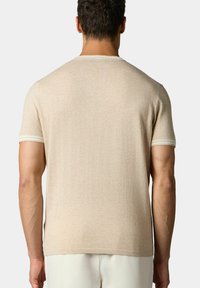 Béžová košile s krátkým rukávem a hladkou texturou. Disponuje kulatým výstřihem a jemnými bílými pruhy na okrajích rukávů. Zobrazeno ze zadní strany.