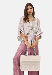 Conjunto de mezcla de algodón que incluye una blusa estampada y pantalones rosas holgados. Un bolso tote beige con el logo "NKN" y un diseño floral completa el look.