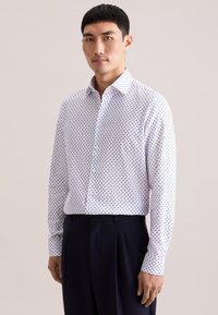 Wit overhemd met blauwe polka dots, lange mouwen, knoopsluiting bij de kraag en een losse pasvorm. Gecombineerd met donkerblauwe broek voor contrast.