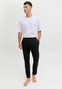 Bílý tričko s krátkým rukávem v kombinaci s černými tapered joggery s elastickým pasem a značkovým akcentem, nošeno naboso.