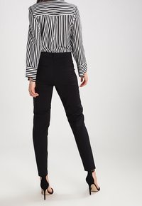 Svart tajta byxor som kombineras med en randig blus i svart och vitt, med långa ärmar och knäppning bak. Höga svarta skor syns.