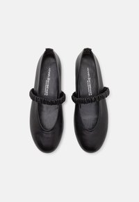 Paire de chaussures plates Mary Jane en cuir noir avec brides élastiques froncées, bouts arrondis et semelles intérieures lisses portant la marque "Kennel Schmenger".
