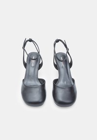 Black leather heeled sandals with a rounded toe and adjustable ankle strap. Smooth texture, minimal design with subtle branding on the insole.