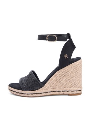 Czarna sandałka na koturnie z plecionym przednim paskiem, paskiem na kostkę z złotą klamrą oraz beżową podeszwą na platformie w stylu espadryli.