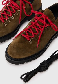 Suede hiking shoes in olive green with rugged black outsole, featuring bright red laces and metallic eyelets. Includes extra black laces.