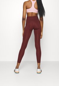Maroon high-waisted leggings made of stretchy material, paired with a pink racerback sports bra. The leggings feature a smooth, sleek design.
